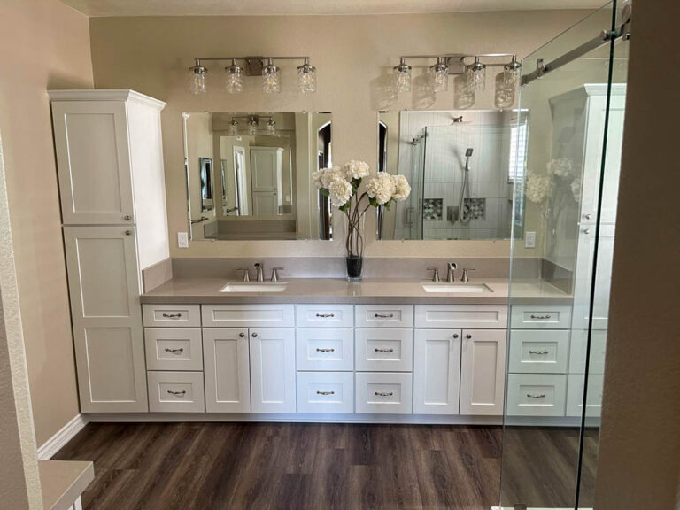 This modern bathroom sanctuary boasts a double vanity with sleek vessel sinks atop a beautiful quartz countertop. The polished chrome faucets add a touch of shine, while the white cabinets create a sense of calmness in the space. Wall-mounted light fixtures provide ample task lighting, while the large mirror reflects natural light, making the room feel even more spacious.