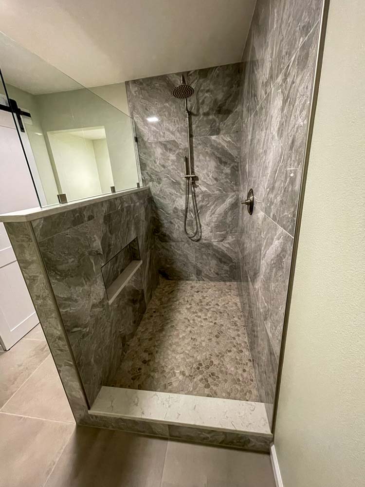 This image features a modern shower enclosure with a clear glass door and gray marble tile surround. The showerhead is mounted on the wall, and the walls appear to have a niche for storing toiletries. The clean lines and gray color scheme create a sense of luxury and serenity in this bathroom haven.